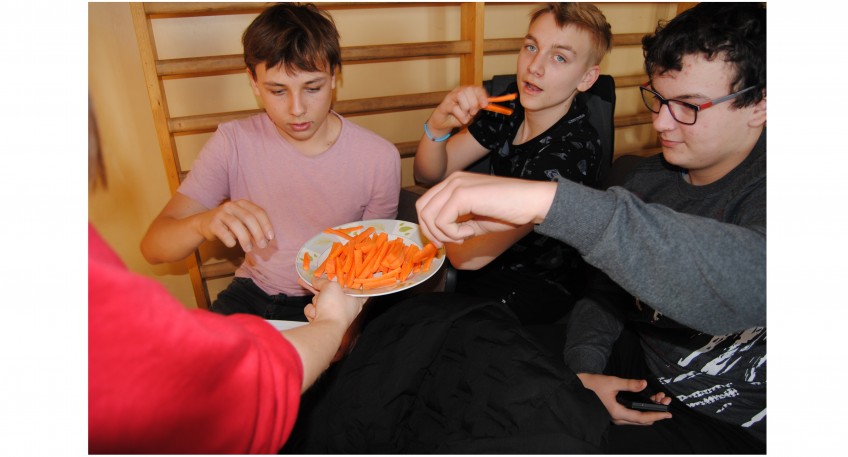 Trójka uczniów bierze pokrojone marchewki z talerzyka.