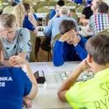 Młodzież siedząca w parach na przeciwko siebie przy stołach i grająca w warcaby