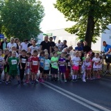 Dzieci na stracie biegu dziecięcego Szamotulskiej Nocnej Piątki, ubrane w kolorowe, sportowe stroje, w tle rodzice dzieci i drzewa 