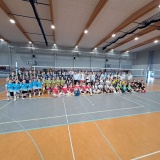 9 drużyn w kolorowych, sportowych strojach, ustawione pod siatkami do gry, pomiędzy zawodniczkami goście meczu