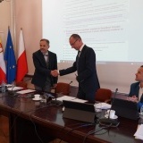 Przewodniczący Rady Powiatu Radosław Łanoszka gratuluje Wicestaroście Rafałowi Zimny, w tle rzutnik z wyświetlonymi informacjami z sesji rady