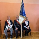 3 uczniów w poczcie sztandarowym w Zespole Szkół Specjalnych w Szamotułach, siedzą na krzesłach pod ścianą 