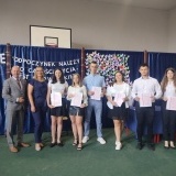 Zakończenie roku szkolnego w Zespole Szkół nr 2 we Wronkach, dyrektor  Sławomir Barszczewski, nauczycielka oraz 6 uczniów z wyróżnieniami na tle grantowej kotary  